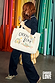 Cream Choose Love Tote Bag featuring colourful illustrations, styled with a navy pinstripe suit in a vibrant studio.