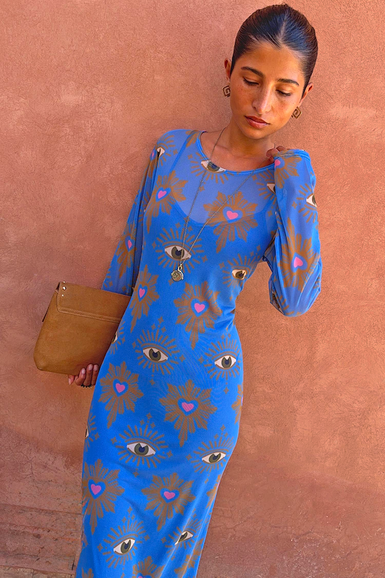 Blue Eye Mesh Dress Petite, a fitted maxi with heart and eye motifs on a model against a terracotta wall.