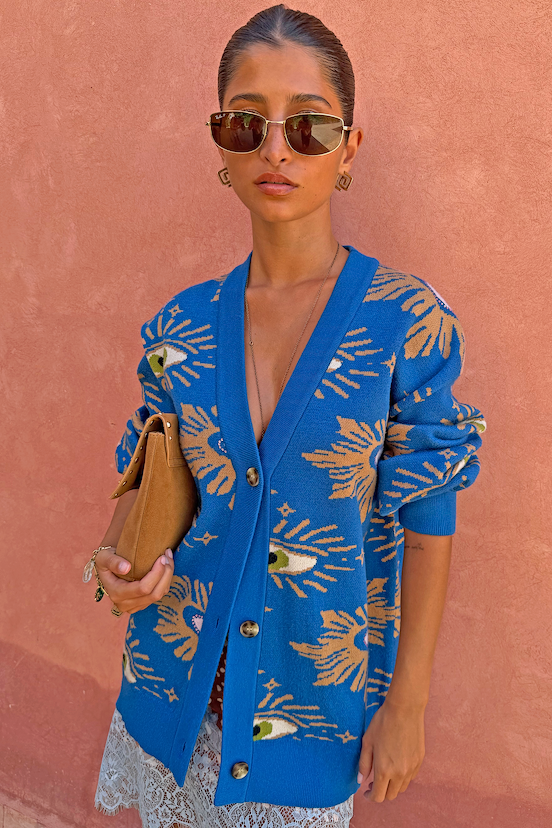 Blue Eye Cardigan with an iconic eye motif and heart illustrations, layered over a lace dress against a pink wall.