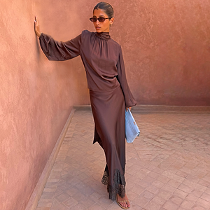 Chocolate Tie Neck Blouse and Chocolate Maeva Skirt with black lace trim on a model in a warm courtyard.