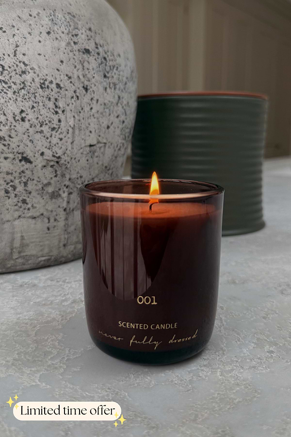 Lit NFD Eau De Parfum Candle 001 in a dark burgundy glass vessel with gold lettering and a flickering flame.