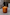 Thumbnail for Lit NFD Scent 002 Candle in a warm orange glass jar with gold branding, set on a textured marble-style surface.