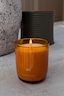 Lit NFD Scent 002 Candle in a warm orange glass jar with gold branding, set on a textured marble-style surface.
