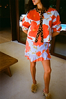 Blue Poppy Cardigan with bold orange poppy print and leopard trim, worn with a matching ruffled wrap skirt.