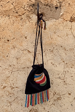Black Banana Pouch Bag with a colourful beaded banana motif and multicolour fringe hanging on a rustic stone wall.