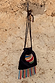 Black Banana Pouch Bag with a colourful beaded banana motif and multicolour fringe hanging on a rustic stone wall.