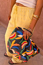 NFD banana print pouch with a black wrist strap, held by a model wearing studded yellow and white striped trousers.