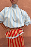Thumbnail for Blue Stripe Batwing Blouse with a high neck and shirred cuffs, paired with a red and tan striped ruffled skirt.