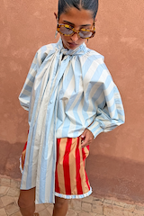 Blue Stripe Batwing Blouse with a high tie neck and voluminous sleeves, styled with red and tan striped shorts.