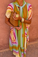 Bright Geo Stevie Maxi Dress featuring colourful geometric stripes and a scarf-tie neck, styled with a tan suede clutch.