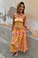 Check Lola Mid-axi Dress in yellow, pink and orange with a ruched bodice and cotton skirt against a textured wall.