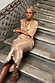 Gold Plisse Dress with angel sleeves and pleated detailing, worn by a model sitting on stone stairs.