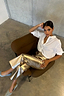 Metallic Gold Vegan Leather Trousers styled with a white shirt on a model seated in a brown armchair.