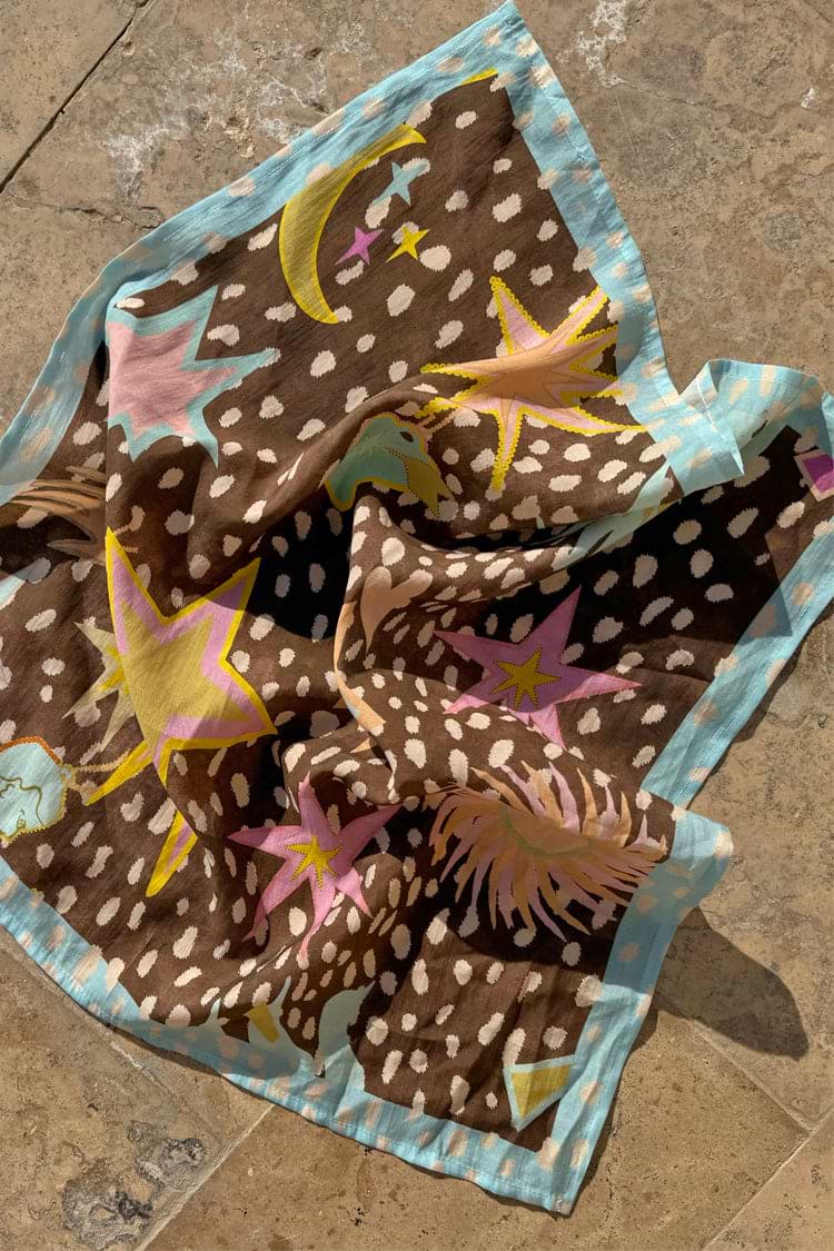 Star Fawn Bandana with a brown fawn spot print and sun, star and palm motifs, displayed on a stone floor.