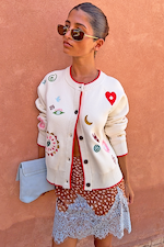 Morocco Charms Cheryl Cardigan in cream with red trim and embroidered motifs, styled on a model with a blue clutch bag.