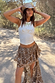 White Cowgirl Tank in cream ribbed fabric, paired with a brown bandana skirt and cowboy hat on a sunlit path.