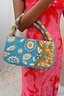 Blue and Yellow Morocco Beaded bag with hand-embellished gold motifs, held by a model in a pink patterned dress.