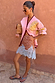 Pink Mystical Cardigan with a gold sun jacquard motif and burgundy trim, styled with a spotted lace-trim skirt.