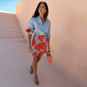 Blue Poppy Mini Jaspre wrap skirt with a bold floral print and frill hem, styled with a light blue shirt.