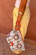 Detachable sun print pouch with a red wristlet strap, paired with yellow striped trousers for vacation styling.