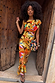 Rio A-Symmetric Top in a colour-block fruit print jersey with a gathered waist, styled as a co-ord in a wooden doorway.