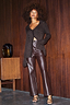 Thumbnail for Brown Vegan Leather Trousers with a straight leg, styled with a shimmery knit top against a wood-panelled wall.