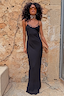 Black Sapna Petite maxi dress with ring detail neckline, styled with a spotted clutch against a stone wall.