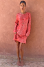 Spliced Fawn Mini Nola Tie Dress in red animal print with long sleeves, worn by a model against a terracotta wall.