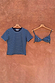 Blue Stripe Bra Baby T-Shirt with a detachable bra overlay, hanging on wooden hangers against a textured wall.