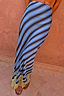 Blue diagonal Stripe Maeva midi skirt with yellow lace trim, shown against a textured terracotta wall.
