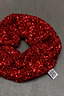 Thumbnail for Red Sequin Scrunchie with shimmering red sequins and a signature white brand logo tag on a grey surface.
