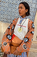 Blue Cotton Stripe Bandana in blue and red, tied around the neck and layered with a sun-motif cardigan.