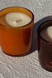 NFD Eau De Parfum Candle 002 in an orange glass jar, displayed on a textured white surface in bright natural sunlight.