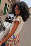 Cream knit Banana Tank with yellow contrast stitching, layered over a colourful abstract print skirt on a city street.