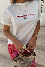 White cotton Rodeo T-Shirt with red slogan text, paired with pink patterned trousers and statement rings.