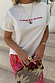 White cotton Rodeo T-Shirt with red slogan text, paired with pink patterned trousers and statement rings.