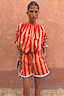 Tomato Stripe Ellie Shorts in red and camel cotton co-ord with contrast hem trim against a textured wall.