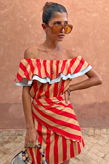 Tomato Stripe Scarf in red and tan styled as a multi-wear ruffled top against a terracotta wall.