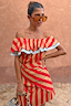 Tomato Stripe Scarf in red and tan styled as a multi-wear ruffled top against a terracotta wall.