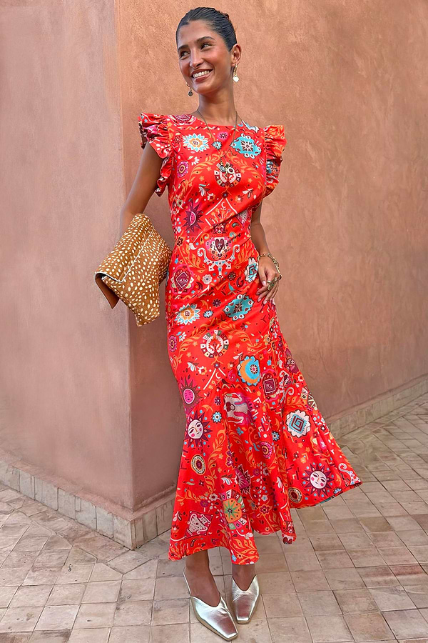 Tomato Tapestry Frida midi dress in red with sun motifs, ruffle sleeves and a fluted hem on a model.
