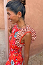 NFD Tomato Tapestry Frida Dress in red with sun motifs, florals and contrasting spot print frill sleeves on a model.