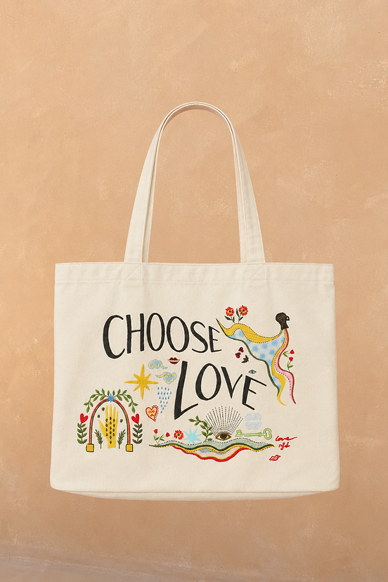 Choose Love Tote Bag in cream recycled cotton featuring colourful graphic artwork and black text against a tan wall.