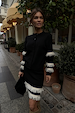model is wearing a black cardigan and skirt with cream fringe detailing on the sleeves and skirt hem