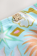 Blue Dreamer High Waist Brief detail with a gold metal NFD logo and sun and palm motifs on blue swim fabric.