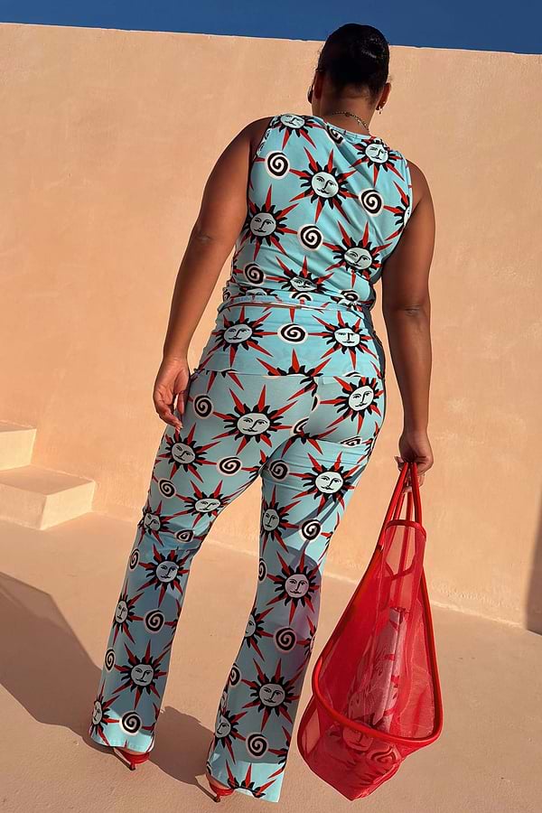 Blue Sun Foldover Trousers in a bright sun and swirl print co-ord, shown from behind on a model with a red mesh bag.