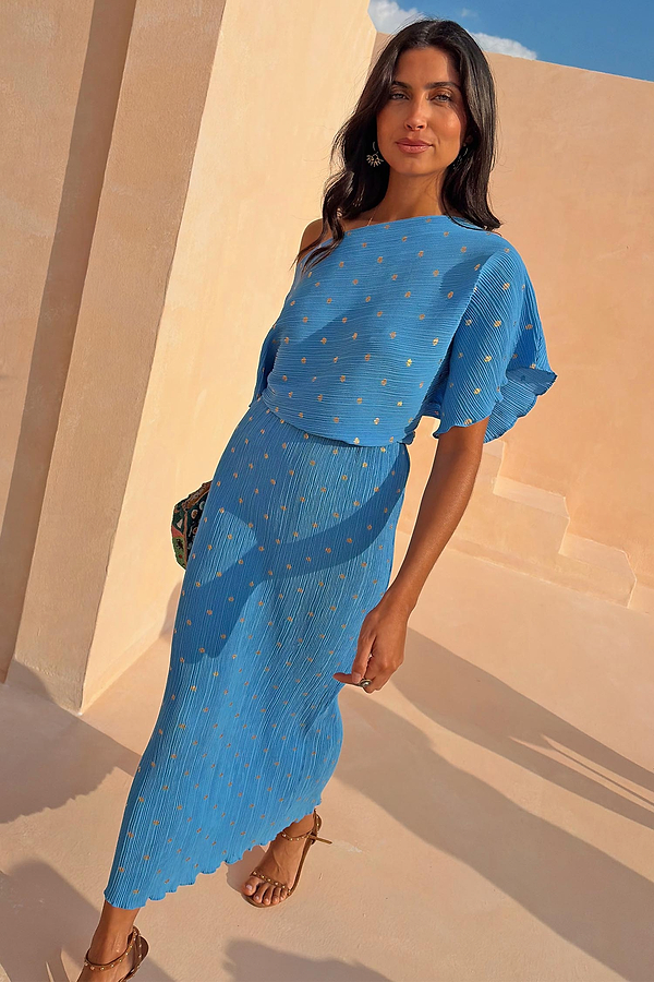 Vibrant blue Plisse Tilly Dress with gold fleck detailing and a draped neckline on a model in the sun.