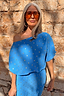 Thumbnail for Blue Plisse Tilly Dress with gold fleck detailing and a draped neckline, worn by a model against a stone wall.