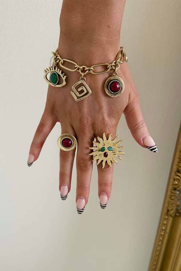 Brushed gold Deloris Charm Bracelet with eye and stone charms, styled on a hand with matching sun and stone rings.