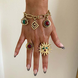 Brushed gold Deloris Charm Bracelet with eye charms, styled with statement sun and stone rings on a hand.