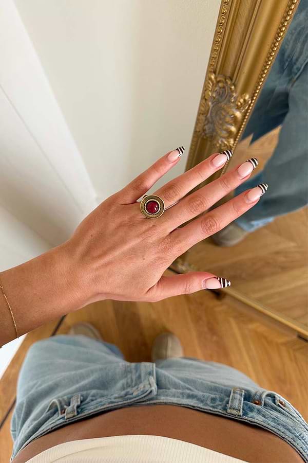 Textured brass Deloris Red Circle Ring with a red semi-precious stone, worn on a hand over light-wash jeans.